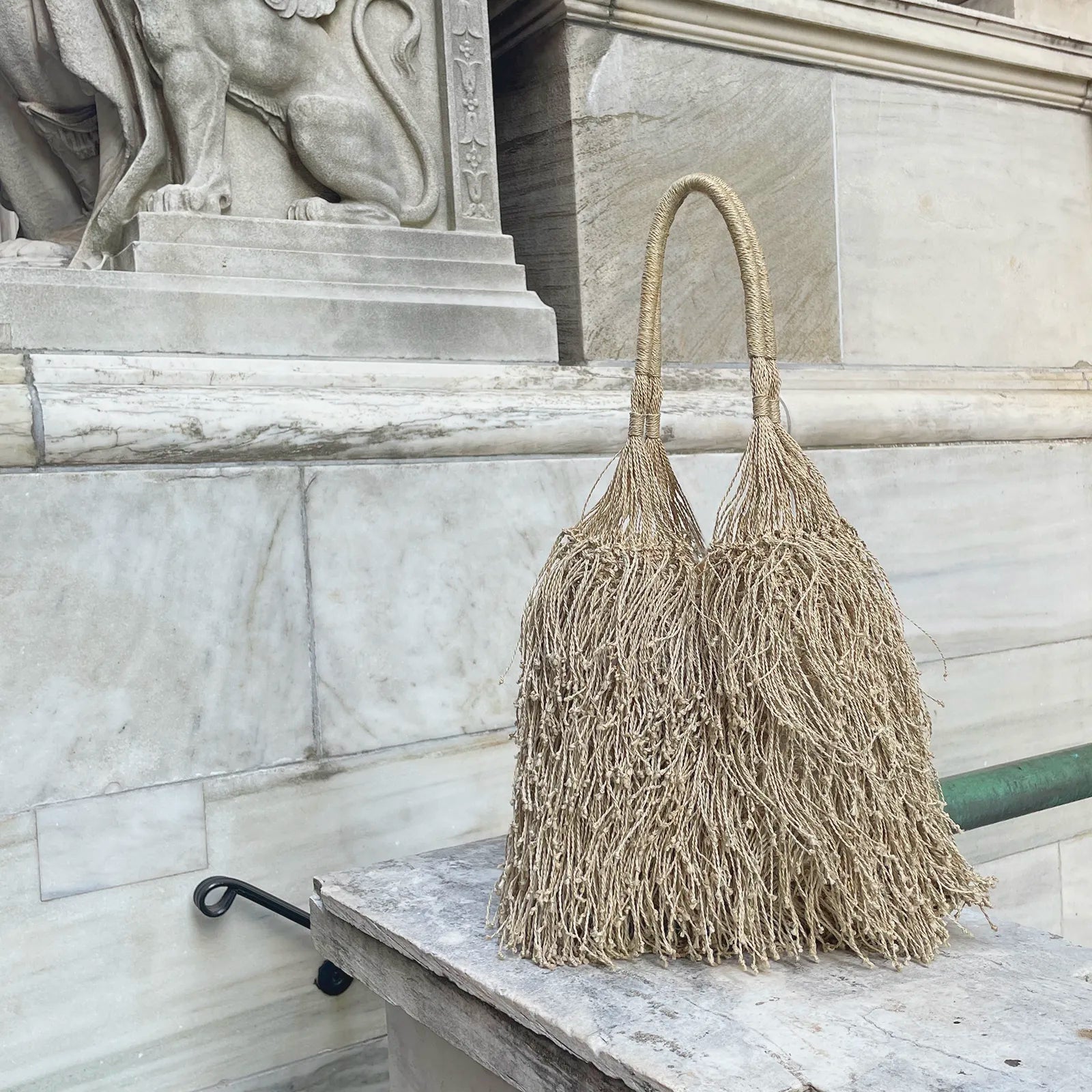 Textured handbag with tassels on a marble surface with a statue in the background