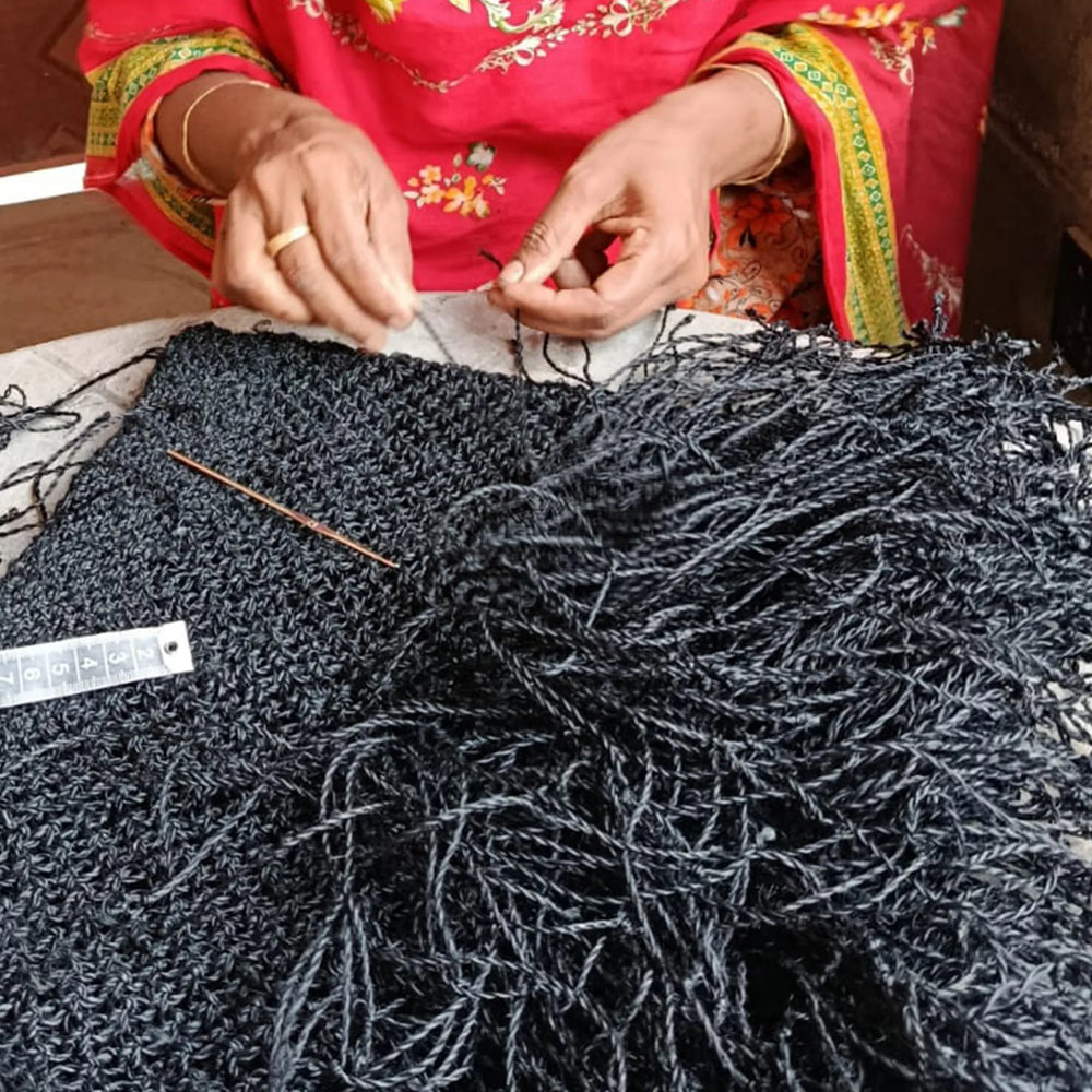 Person knitting with dark yarn and knitting needles, wearing a red garment with gold embroidery.