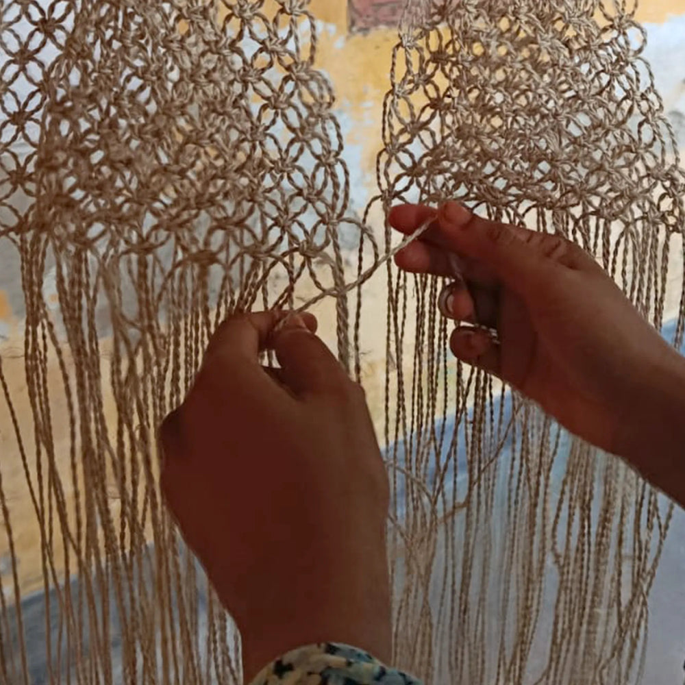 Handmade macrame wall hanging with hands working on it.