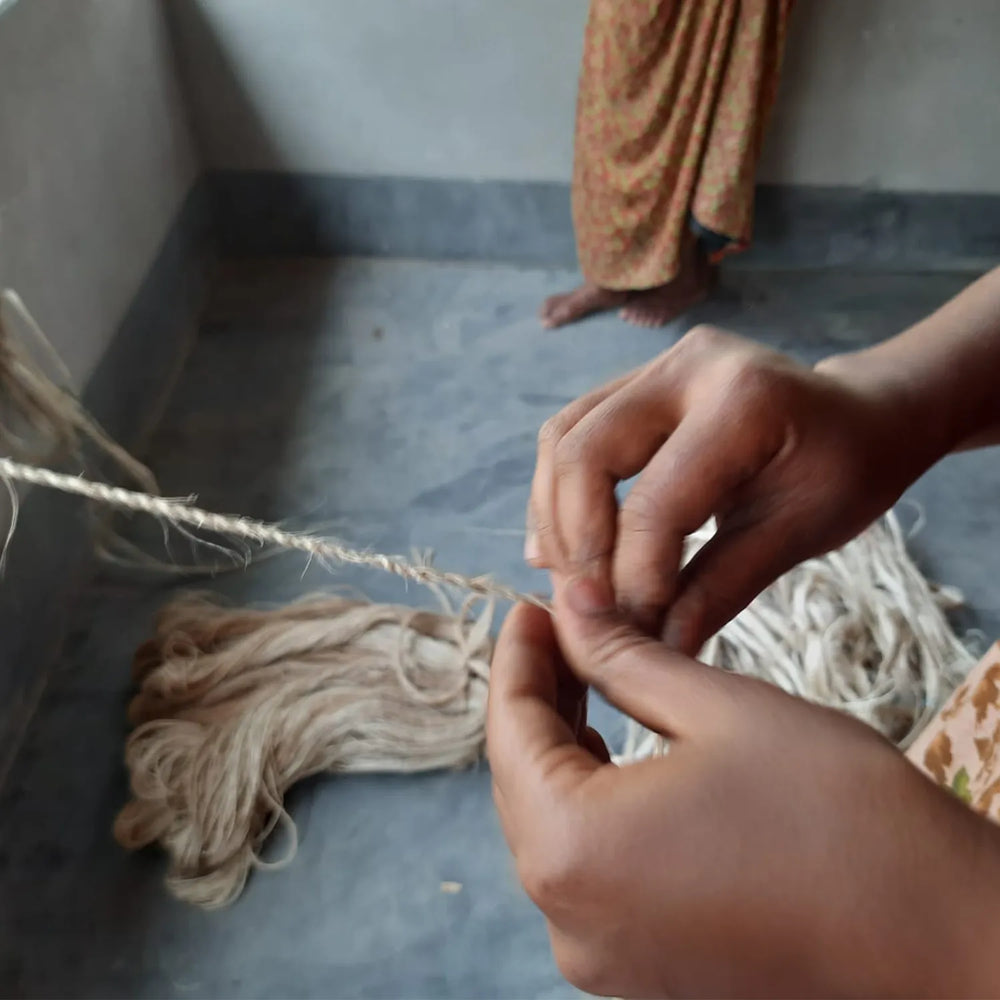 Close-up of hands working with yarn on a concrete floor.