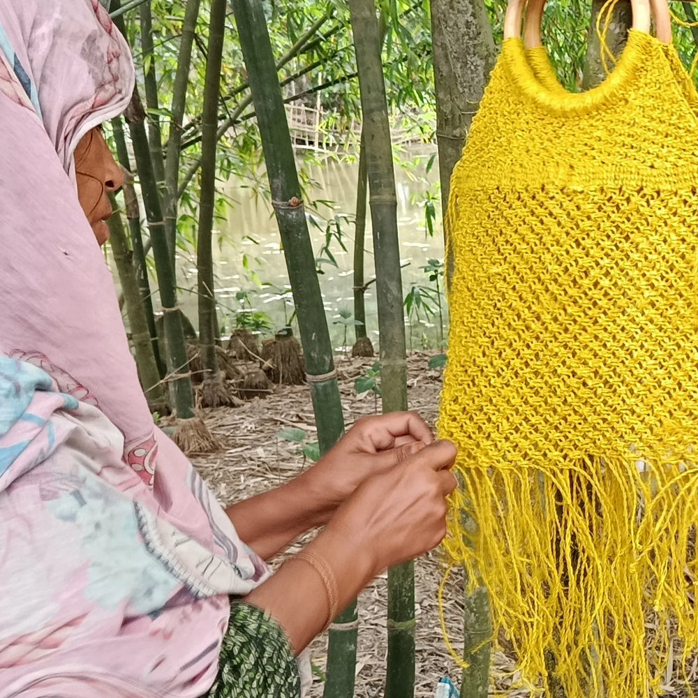 Person holding a yellow woven bag in a natural setting with bamboo trees.