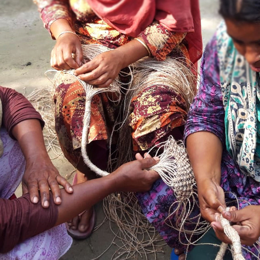 Three women sitting on the ground, working with fishing nets.