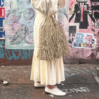 Person wearing a long white dress and holding a textured bag against a colorful mural background.