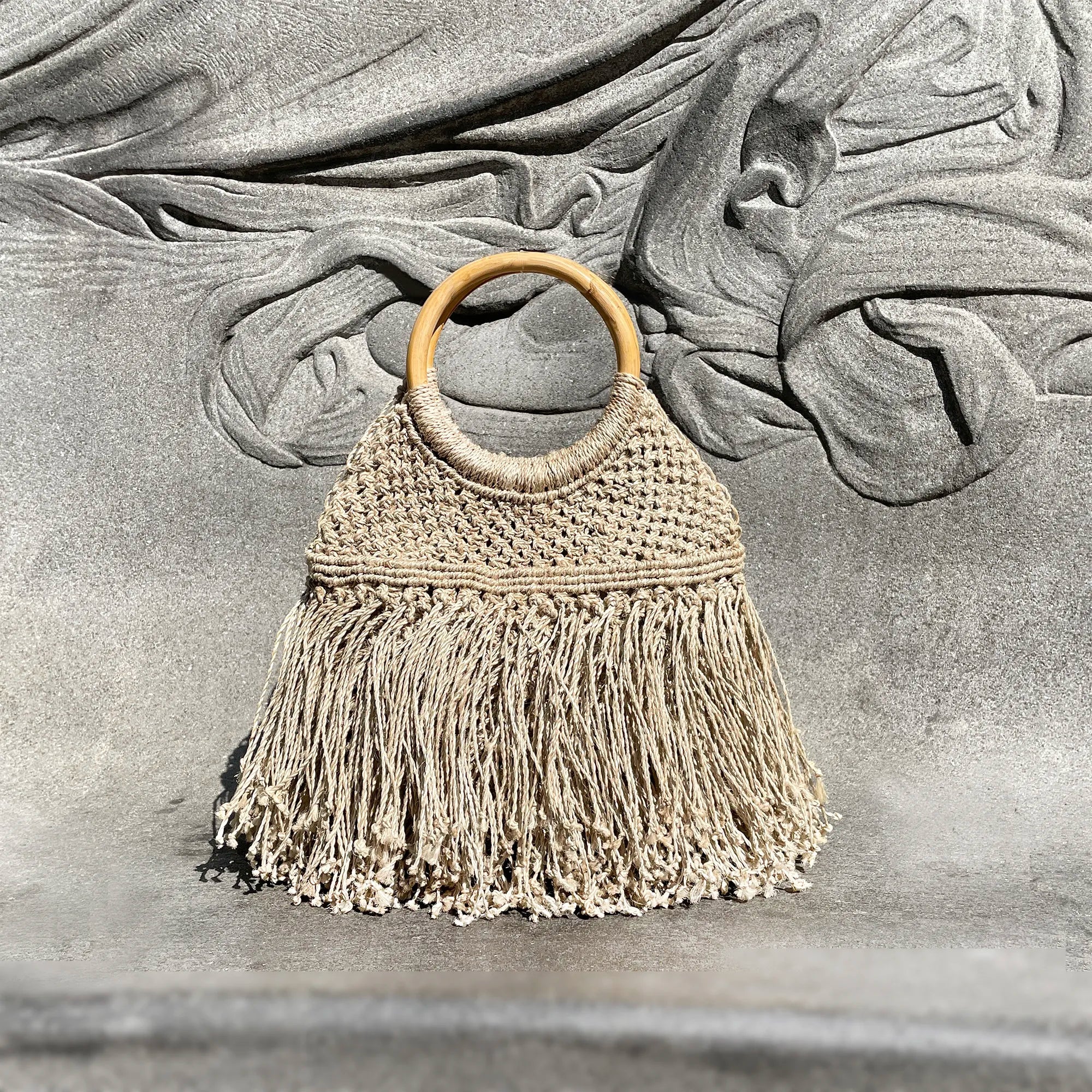 Macrame handbag with wooden handle and fringe on a textured stone background